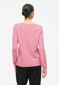 Light pink sweater in a soft knit material, featuring long sleeves, a round neckline, and ribbed hem and cuffs. Plain back design.