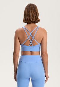 Svetlo modra športna modrček z križnimi naramnicami, gladka tekstura in umestitev logotipa. V kombinaciji z ujemajočimi se visoko pasnimi legicami.