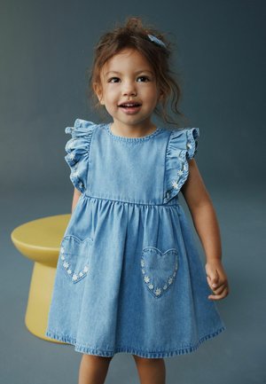 Denimkjole med flæseærmer, rynket talje og hjerteformede lommer med blomsterbroderi. Lyseblå farve, afslappet design.