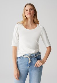 T-shirt blanc à manches longues avec un col rond ; tissu doux et lisse ; associé à un jean bleu clair avec une taille à cordon.