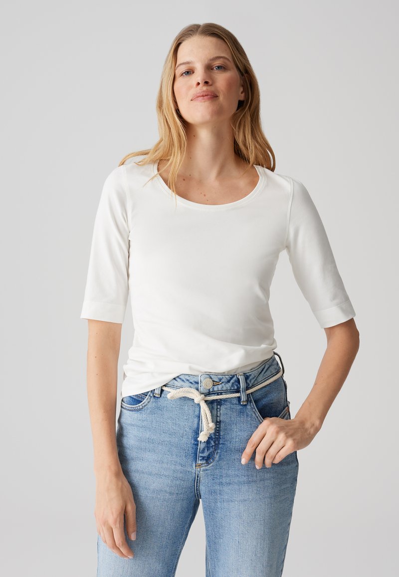 T-shirt blanc à manches longues avec un col rond ; tissu doux et lisse ; associé à un jean bleu clair avec une taille à cordon.