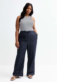 Pantalons en denim à jambe large avec taille élastiquée, de couleur bleu profond, et poches latérales, associés à un haut sans manches à rayures noir et blanc.