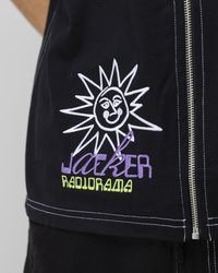 Black fabric jacket featuring white and colorful embroidery of a sun design and the text "Jacker Radiorama," with visible silver zipper detail.