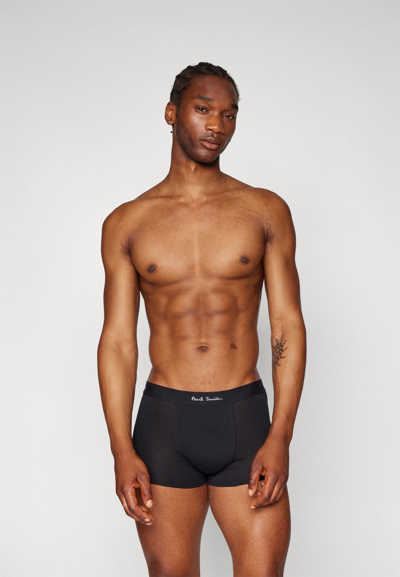 Boxers noirs en coton avec une taille élastique estampillée. Le mannequin a une silhouette athlétique, mettant en avant l'ajustement et la texture du tissu.