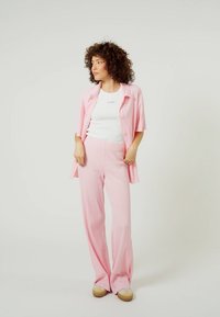 Růžová žebrovaná košile na knoflíky a odpovídající rozšířené kalhoty, s bílým fitted tričkem pod ní a světlými botami.