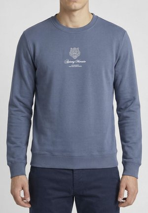 Uomo con felpa blu girocollo con grafica di tigre bianca e testo "Antony Morato Established Two Thousand Seven" sul petto.