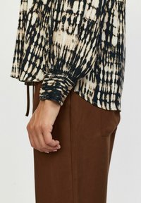 Fekete és bézs batikolt mintájú hosszú ujjú bl�úz, gombos mandzsettával és laza fit-tel. Barna nadrággal párosítva.