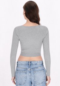 Szürke bordázott crop top hosszú ujjakkal és kerek nyakkivágással, magas derekú világoskék farmernadrággal párosítva.