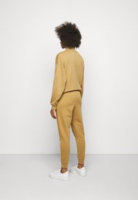 Khakifarbene Sweatshirt- und Jogginghose-Set aus weichem Stoff, mit lockerer Passform, langen Ärmeln und gerippten Bündchen, kombiniert mit weißen Sneakers.