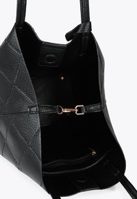 Innenseite einer schwarzen Lederhandtasche, die die gesteppten Texturen, ein Reißverschlussfach und einen goldenen Verschluss zum Sichern des Inhalts zeigt.