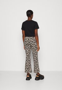 T-shirt noir associée à un pantalon évasé à imprimé léopard avec un fond crème et des taches marron foncé, complétée par des sandales noires épaisses.