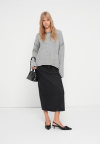 Maglione grigio a maglia con maniche raglan, gonna midi in denim nera, décolleté neri con cinturino alla caviglia e piccola borsa nera.
