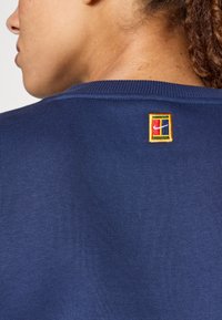 Μπλούζα ναυτικού μπλε με ραμμένα μανίκια, που διαθέτει ένα μικρό πολύχρωμο κεντημένο λογότυπο σε ορθογώνια ετικέτα στην πλάτη.