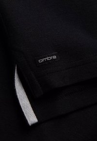 Černá texturovaná tkanina s bílým vnitřním švem; obsahuje malou černou št ítek se slovem "ombre" vyšitým na něm.