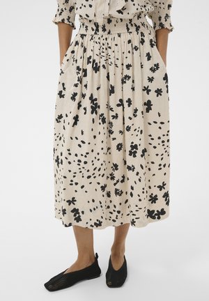 Jupe midi beige à imprimé floral noir, taille élastique et poches latérales, portée avec des chaussures noires en mesh sans lacets.