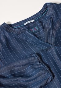 Camicia a righe blu con scollo a V e maniche arricciate. Realizzata in cotone, con una superficie liscia e una leggera lucentezza. Etichette visibili.