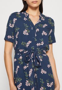 Navy floral dress with short sleeves, v-neck, and buttons. Features a belted waist and a pattern of pink flowers and green leaves.