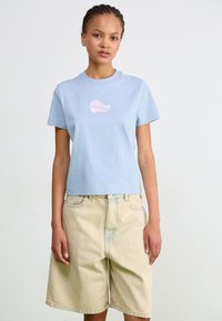 Ljusblå bomullströja med en rosa snäcka-graphic på bröstet, ihopparad med beige denimshorts med avslappnad passform och framträdande fickor.