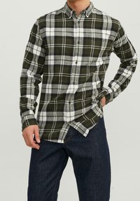 Camicia a quadri verde e bianca con bottoni, colletto, maniche lunghe e taglio dritto. Indossata con jeans denim scuro. Presenta bottoni sulla parte anteriore.