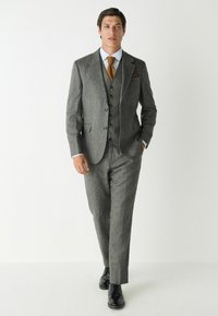 Gray tweed three-piece suit with notch lapels, buttoned vest, and brown tie. Slim fit trousers and black dress shoes. Elegant and classic design.