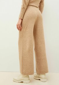 Un pantalon large beige en tissu doux et texturé, doté d'une taille haute et associé à des bottes à lacets de couleur crème.