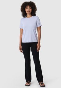 Světle levandulové tričko s krátkými rukávy, kombinované s černými rozšířenými kalhotami a černými sandály. Hladká látka, jednoduchý design, žádné viditelné vzory.