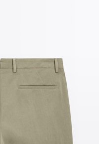 Khakifärgade byxor av texturerad tyg, med slät front, bältesloops och en enda bakficka med en subtil sömnadsdetalj.