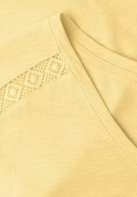 Tissu jaune avec un décolleté en V et un panneau en dentelle décoratif présentant des motifs en forme de losange.