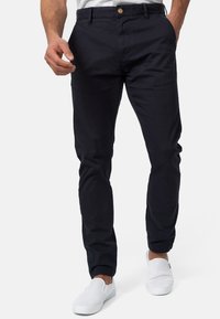 Chinos de algodón de corte ajustado en color azul marino con cinturilla abotonada y bolsillos laterales. Combinados con zapatos blancos de tipo slip-on.