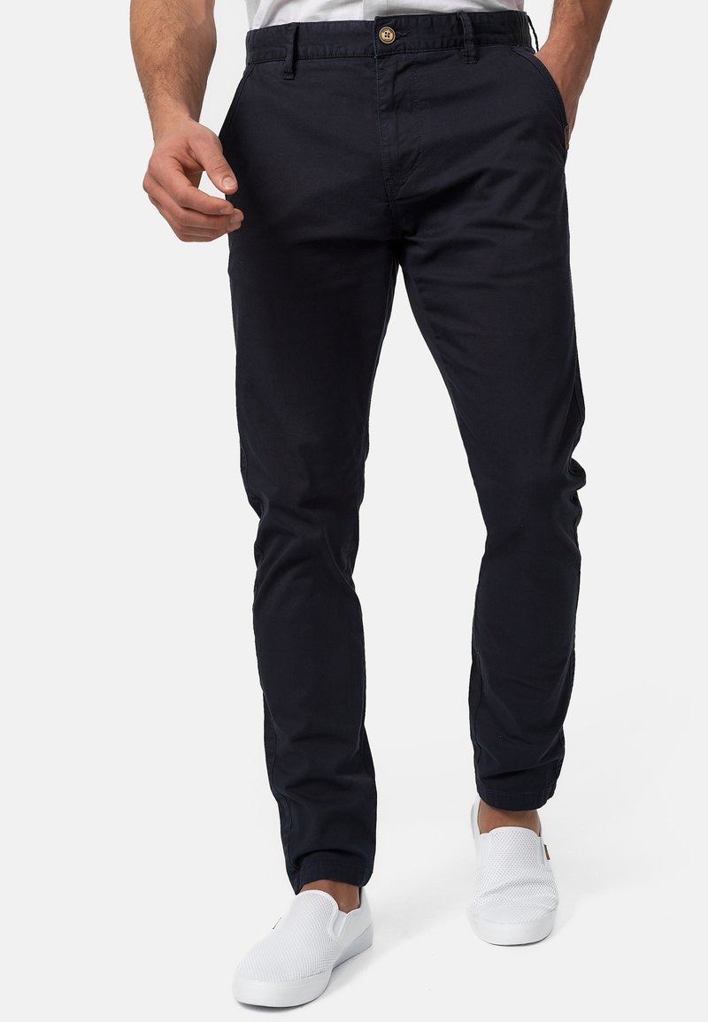 Chinos de algodón de corte ajustado en color azul marino con cinturilla abotonada y bolsillos laterales. Combinados con zapatos blancos de tipo slip-on.