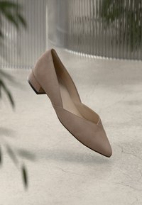 Beige suede low-heeled shoe with a pointed toe and cut-out design on the sides. Smooth texture; solid black heel accent.