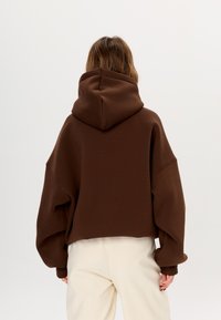 Felpa con cappuccio marrone, dal taglio rilassato e spalle scese, realizzata in tessuto morbido. Presenta un ampio cappuccio e polsini a costine.