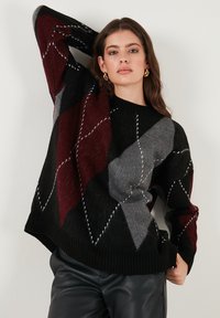 Pulover cu model în nuanțe de negru, roșu și gri, cu un design argyle și accente de cusături albe. Are un guler rib și o croială lejeră.