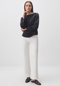 Blusa nera a maniche lunghe con bottoni dorati, pantaloni bianchi a gamba larga, mocassini neri. Tessuto liscio, taglio contemporaneo, design minimalista.