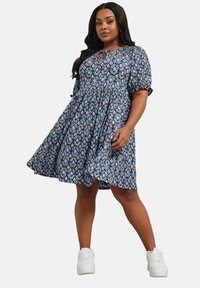 Robe bleue et blanche à motif, avec une coupe décontractée, des manches courtes et un détail d'encolure en forme de clé, associée à des baskets blanches.