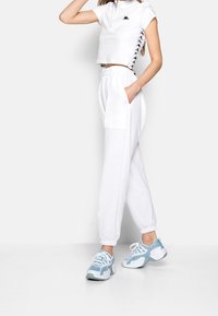 Vit kort topp med dragkedjedetalj och svarta accenter, i kombination med vita smalnade joggers med sidofickor. Blåa sportskor.