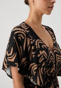 Svart og beige mønstret kjole med dyp V-hals, utsvingte ermer og samlet midje, med abstrakt design og glatt tekstur.