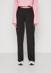 Black wide-leg pants with a smooth texture and a tailored design. Paired with a pink cropped long-sleeve top and white sneakers.