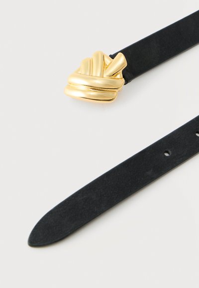 Μαύρη ζώνη από σουέντ με στριφτή, γλυπτική αγκράφα από χρυσό μέταλλο σε λευκό φόντο, μερικώς ανοιχτή και εμφανή τρύπες.