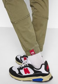 Zwart-witte sport sneakers met rode accenten, gevoerde zolen en een stijlvol ontwerp. Olijfgroene broek met een rood label bij de zoom.