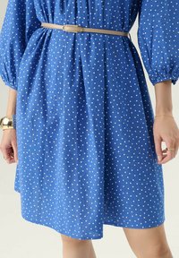 Abito blu a pois realizzato in tessuto leggero, con maniche a palloncino e vita stretta, completato da una cintura di colore chiaro.