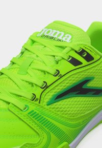 Κοντινό πλάνο αθλητικού παπουτσιού Joma Dribling σε νέον πράσινο με υφή από δίχτυ, κορδόνια και λογότυπο μαύρο-πράσινο στο πλάι.