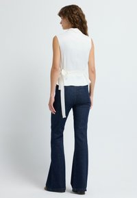 Hvid ærmeløs top med peplumdesign og en bagside med sløjfe, båret med mørkeblå vidde jeans. Glat tekstur og rene linjer.