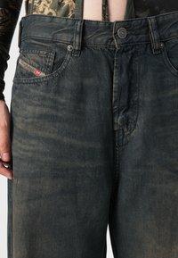Donkerblauwe denim jeans met een licht vervaagde textuur. Beschikt over een voorzak met een klein rood Diesel logo-label en zilveren hardware knopen.