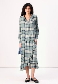 Green and blue plaid dress with long sleeves, ruffled hemline, and a loose fit, featuring button-down front and soft fabric texture.