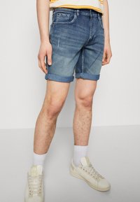 pantalones cortos de mezclilla con un degradado de azul claro a oscuro, con dobladillos enrollados y bolsillos frontales, combinados con calcetines blancos y zapatillas ligeras.