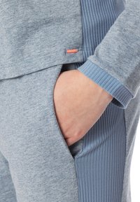 Conjunto de sudadera azul claro que presenta un panel de punto texturizado, ajuste relajado y un bolsillo lateral. Los detalles notables incluyen una pequeña etiqueta naranja.
