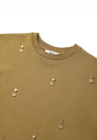T-shirt en coton vert olive avec des accents métalliques ronds disposés de manière aléatoire sur le devant. Encolure ronde classique avec texture côtelée.