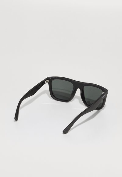 Ochelari de soare negri cu ramă pătrată, lentile gri cu nuanță, și brațe din acetat texturat negru, având un accent metalic aproape de balamale.
