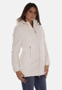 Giacca bianca con zip e cappuccio, caratterizzata da una texture liscia e due tasche laterali con chiusura zip. Progettata con dettagli di cucitura discreti.